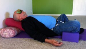 A man lying back on bolsters with his legs bent out to the sides in a passive, restorative yoga pose.