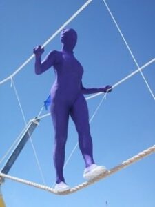Image of a woman in a head to toe purple costume on a slack rope above the ground.