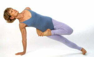 An image of a yoga teacher in a side balancing pose in half lotus
