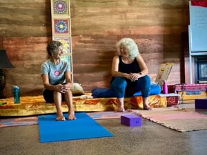 Eve and Libbie teaching yoga at a workshop, seated and laughing