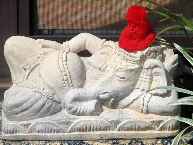 An image of a statue, Ganesha the Hindu God reclining and wearing a beanie.